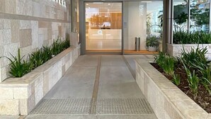 A modern building entrance with a stone facade, a sign reading "SIGNATURE," and a glass door leading inside. - NEW Ocean view 1BR | Pool, Parking & Walk to Beach (Broadbeach)