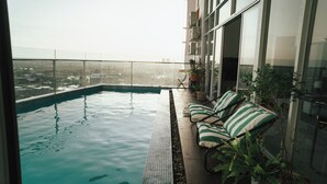 Piscina infinita con vistas despejadas del paisaje urbano, barandilla de cristal y zona de estar con cojines a rayas.