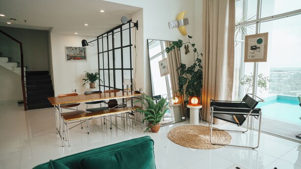 Amplia sala de estar con una mesa de comedor, un sofá verde y vistas a una piscina a través de grandes ventanales.