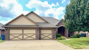 A two-story house with a garage, brick exterior, and a large tree in the front yard. - Heart of Edmond Retreat - 3bed 2bath (Edmond)