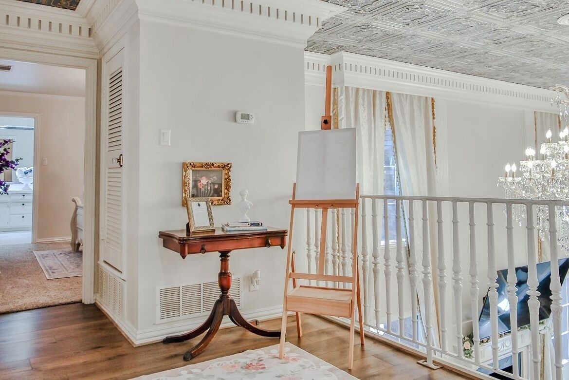 Ein Zimmer mit Holzboden, weißer Wand, weißer Geländer, einer Chandelier und einem Gemälde an der Wand.