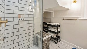 A modern bathroom with a glass shower enclosure, white subway tiles, a towel rack, and a basket.