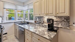 A kitchen with granite countertops, a coffee maker, and a window with blinds.
