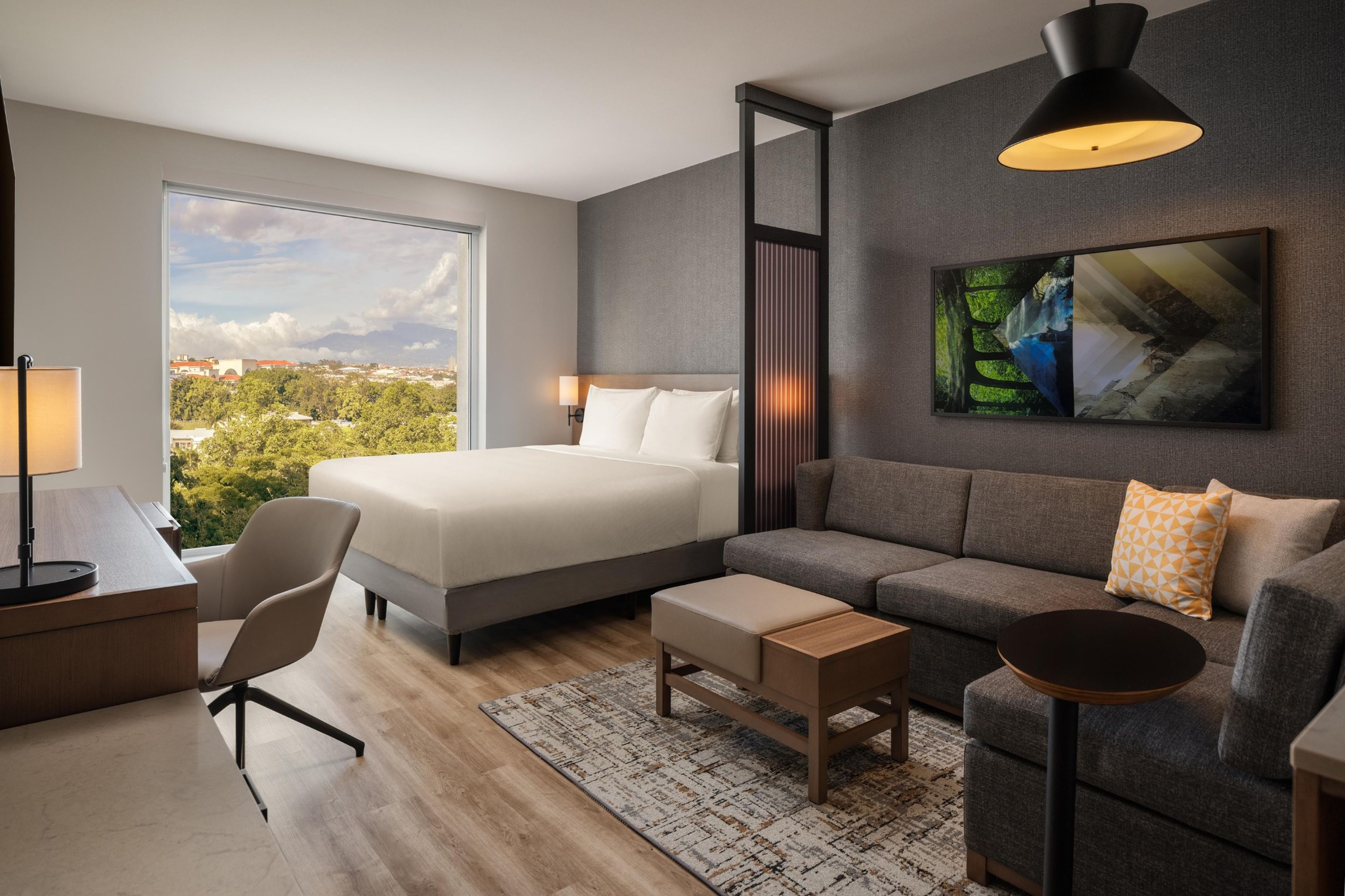Habitación de hotel moderna con una cama grande, un sofá, un escritorio y vistas a la ciudad.