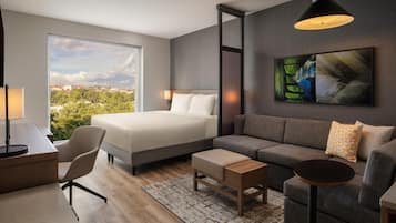 Habitación de hotel moderna con una cama grande, un sofá, un escritorio y vistas a la ciudad.