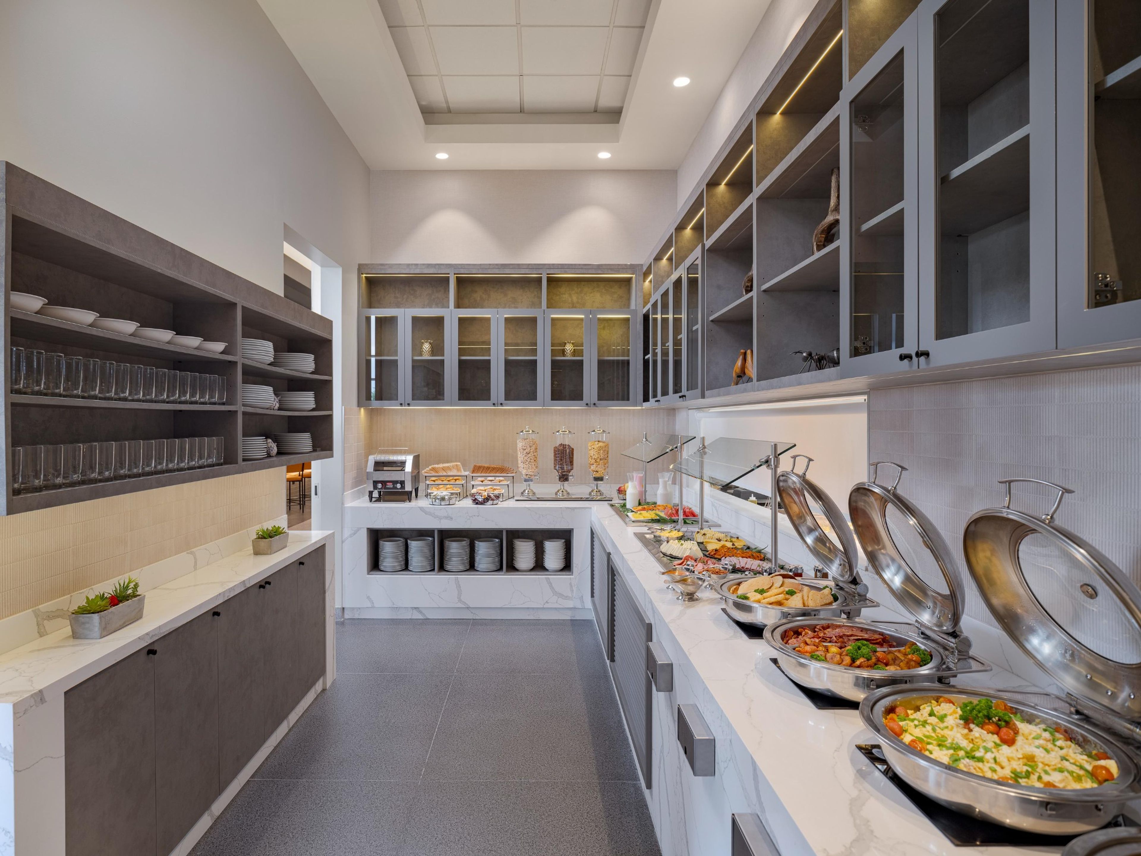 A buffet setup with various food items, a coffee machine, and a seating area with chairs.