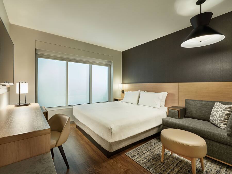 Quarto de hotel moderno com cama, escrivaninha, sofá e uma grande janela.
