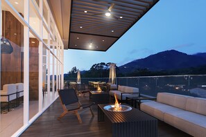 A modern outdoor patio with a fire feature, seating, and a view of mountains. - Hyatt Place Cariari Convention Center (Ulloa)