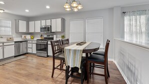 A modern kitchen with white cabinets, a built-in oven, and a dining area with a table and chairs. - Spacious Home Near Coffee and Cedar Park Shopping (Leander)
