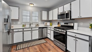 A modern kitchen with stainless steel appliances, white cabinetry, and a wooden floor. - Spacious Home Near Coffee and Cedar Park Shopping (Leander)