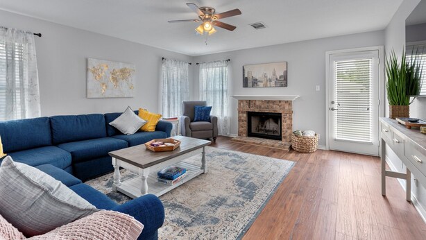 A living room with a blue sofa, a coffee table, a fireplace, and a ceiling fan. - Spacious Home Near Coffee and Cedar Park Shopping (Leander)