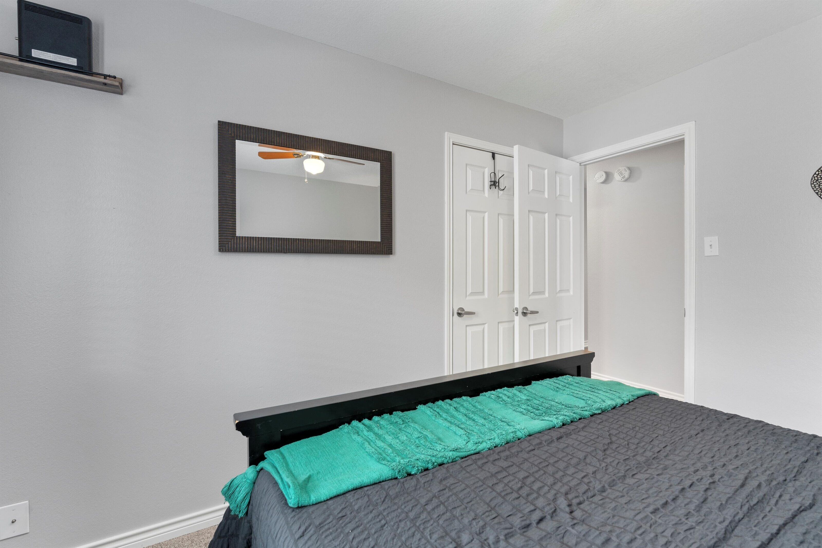 A bedroom with a bed, a white door, a mirror, and a ceiling fan.