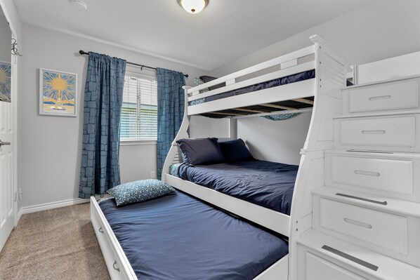 Habitación con literas, ventana, cortinas y una cama con cabecero que funciona como mesita de noche.