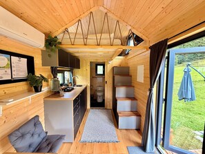 A compact cabin interior with a kitchenette, a seating area, and a view of the outdoors. - The Alpine Experience 2 by Tiny Away (Zell-Freibach)