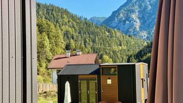 Een klein vakantiehuisje met een rood dak, een houten terras en een witte parasol.