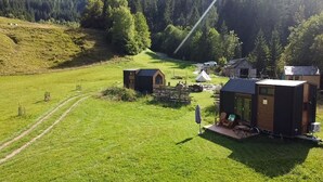 Un entorno rural con una cabaña pequeña, una tienda de campaña y un sendero que atraviesa un campo verde.