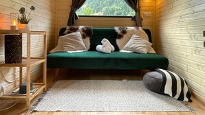 Una habitación acogedora con un sofá verde, una mesita con una vela y vistas a colinas verdes.