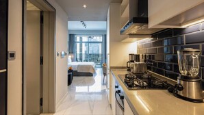 A modern kitchen with a gas stove, a blender, and a coffee maker. There is a large window in the adjacent room.