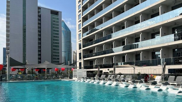 A hotel pool area with multiple levels of balconies, a clear blue pool, and a modern building in the background.