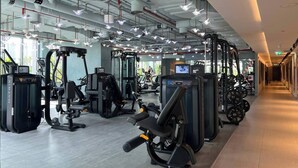 A modern gym with various exercise machines, a long corridor, and a large window providing natural light.
