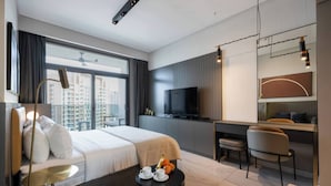 A modern hotel room with a large bed, a desk, a TV, and a balcony with a city view.