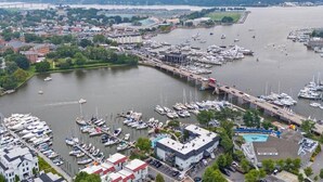 A marina with numerous boats docked, a bridge in the background, and a cityscape with buildings and greenery.