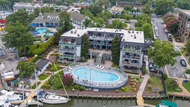 A multi-story building with a pool, surrounded by greenery and a waterfront.