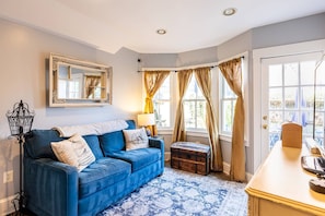 A room with a blue sofa, a wooden chest, a mirror, and a window with curtains.