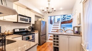 Una cocina moderna con encimeras de granito, electrodomésticos de acero inoxidable y vistas a una escalera de madera que sube a un altillo.
