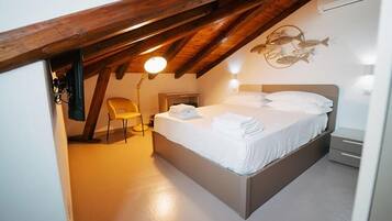 A bedroom with a sloped ceiling, a bed with white linens, a chair, and a wall-mounted light fixture.