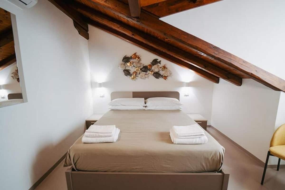 A bedroom with a bed, bedside tables, a wooden ceiling, and a wall decoration.
