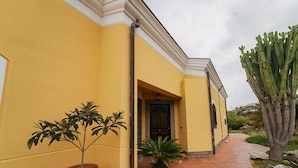 A yellow building with a tiled pathway, potted plants, and a cactus. - B&B Villa Gabry  (Capo d'Orlando)