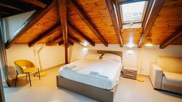 A bedroom with a sloped ceiling, a bed, a chair, a floor lamp, and a sofa.
