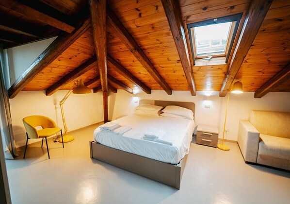 A bedroom with a sloped ceiling, a bed, a chair, a floor lamp, and a sofa. - B&B Villa Gabry (Capo d'Orlando)