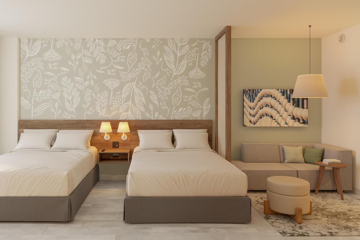 Ein Hotelzimmer mit zwei Betten, einem Schlafsofa, einem kleinen Tisch und einer Wanddekoration.
