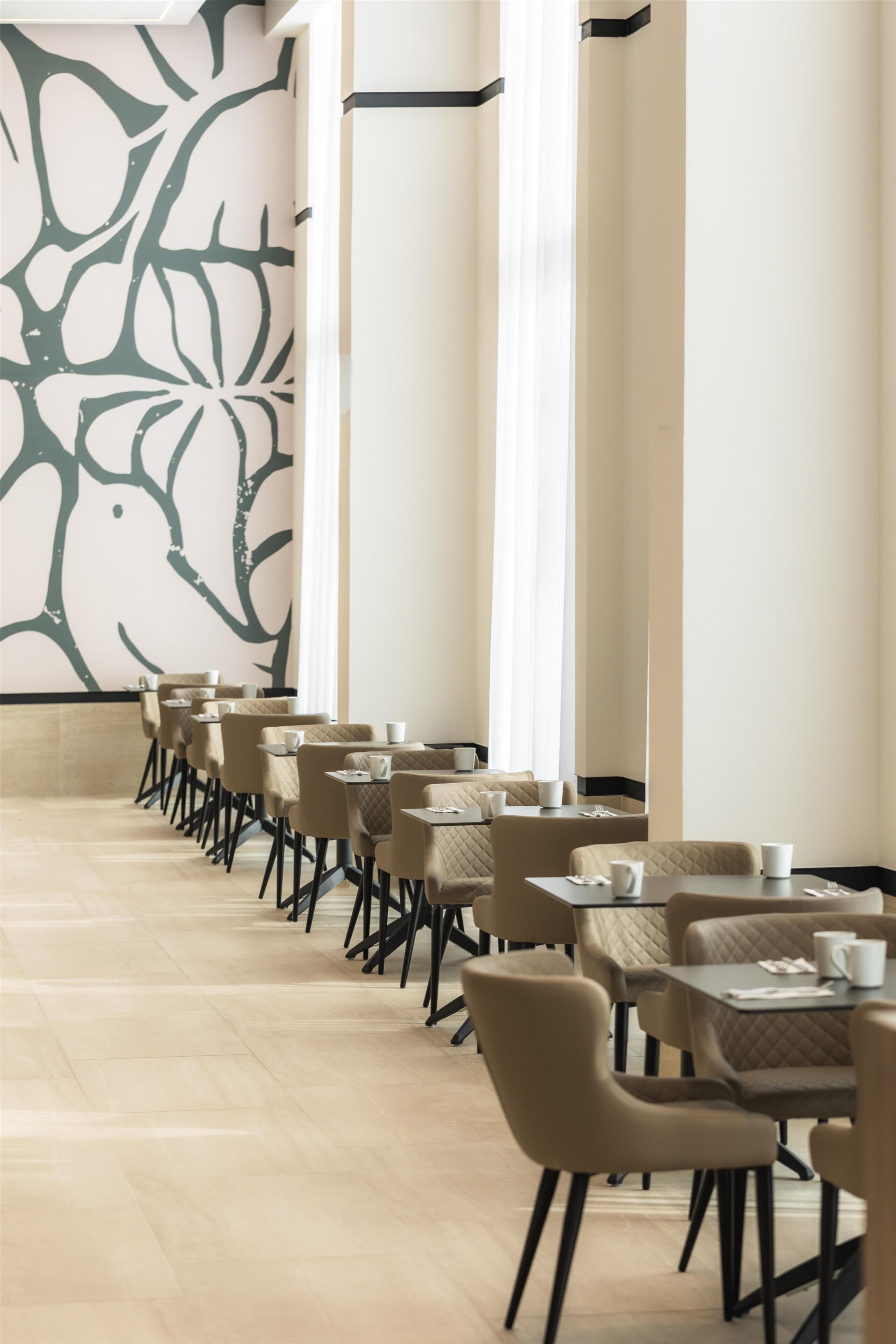 A modern dining area with a long table and chairs, a large abstract mural on the wall, and a tall column in the center.