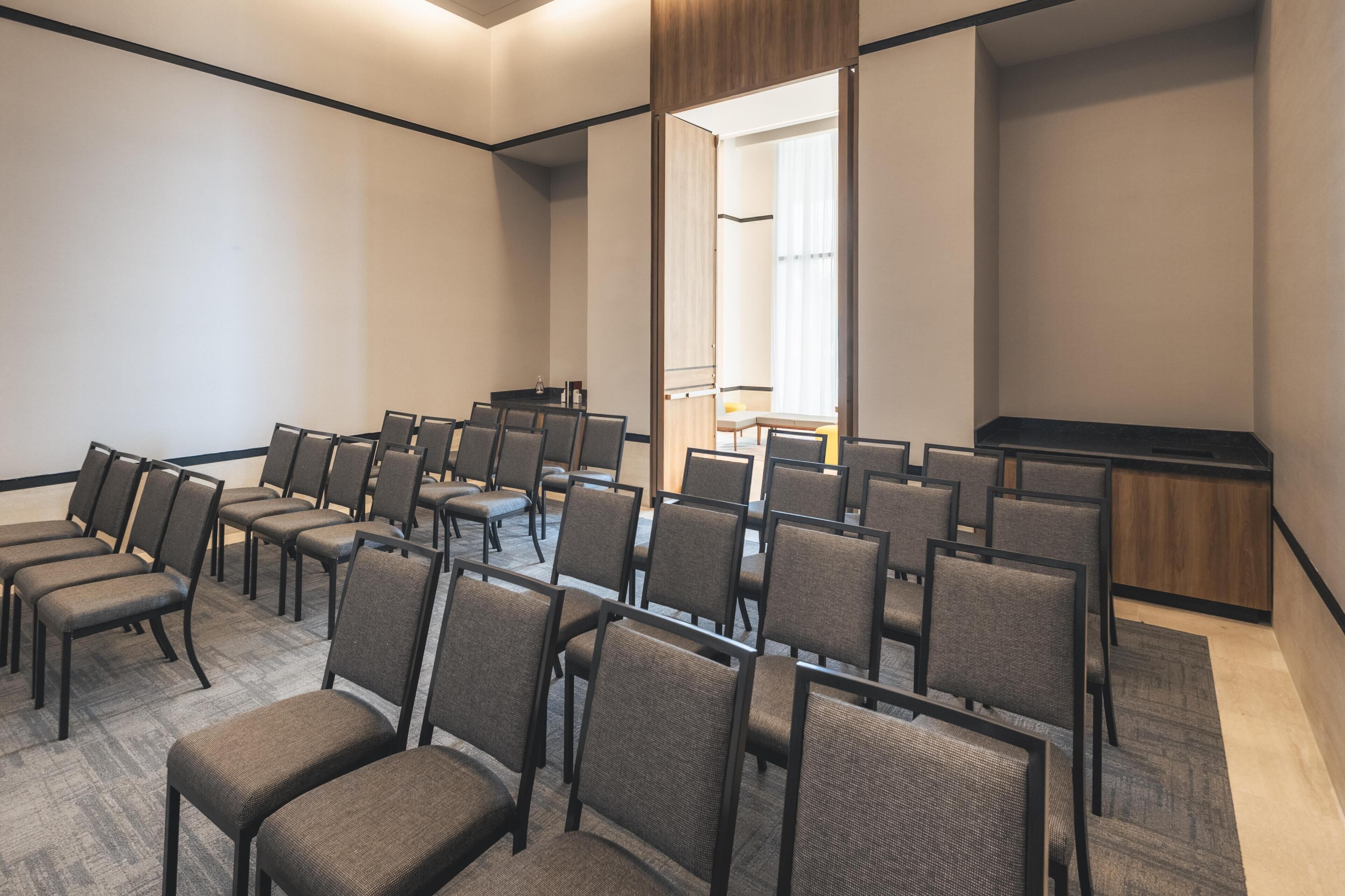Un salón de conferencias con filas de sillas, un atril y un espejo grande en la pared.