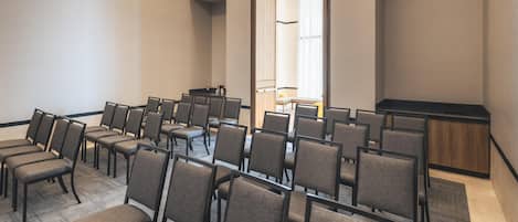 A conference room with rows of chairs, a podium, and a large mirror on the wall.
