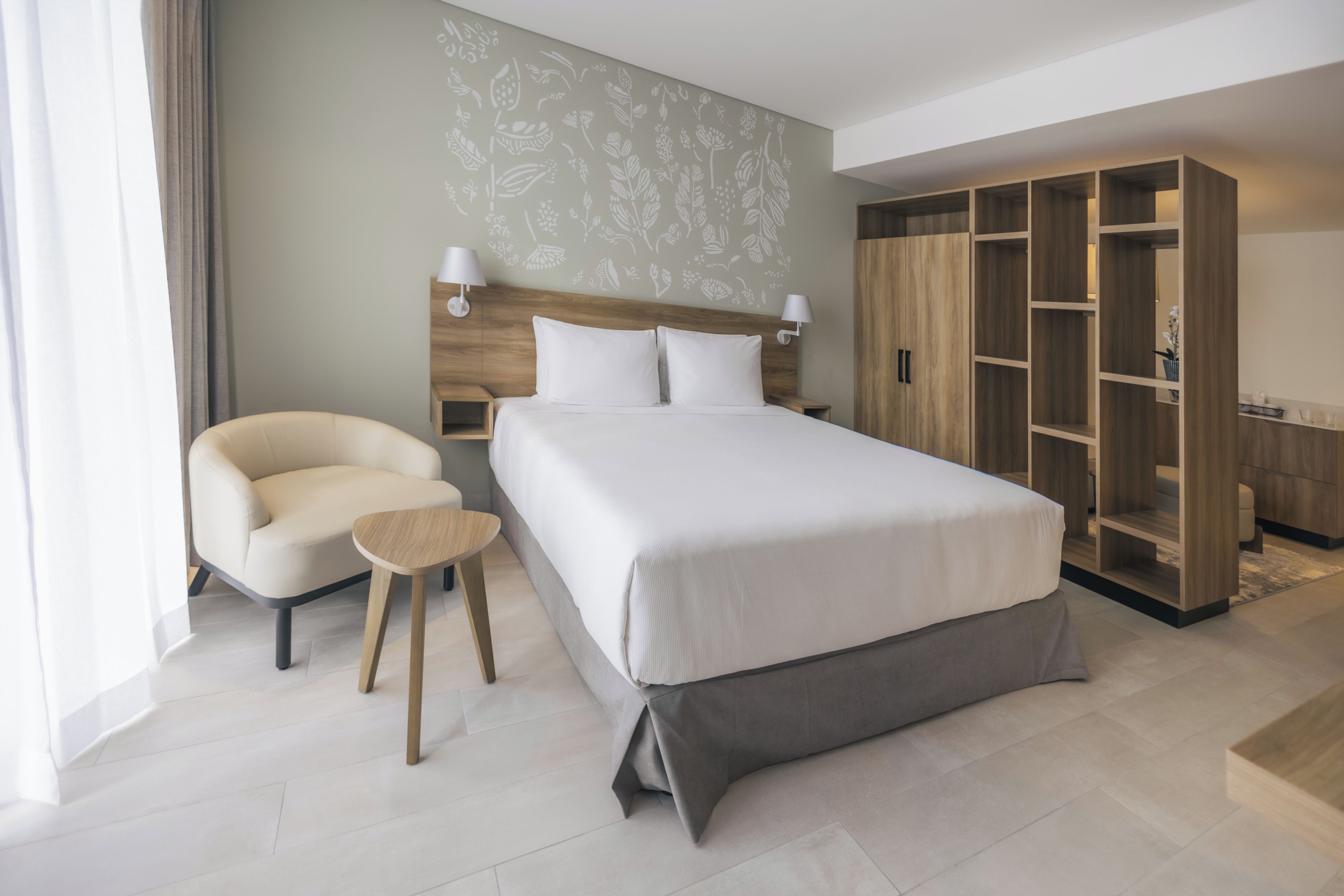 Una habitación de hotel moderna con una cama grande, una zona de estar, un armario y una pared con estampado floral.