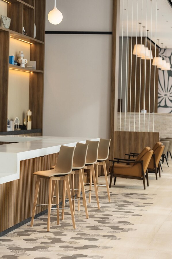 A modern bar area with a white countertop, wooden chairs, and pendant lighting.