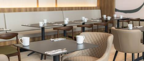 Un comedor moderno con mesas y sillas, algunas con tazas blancas encima.