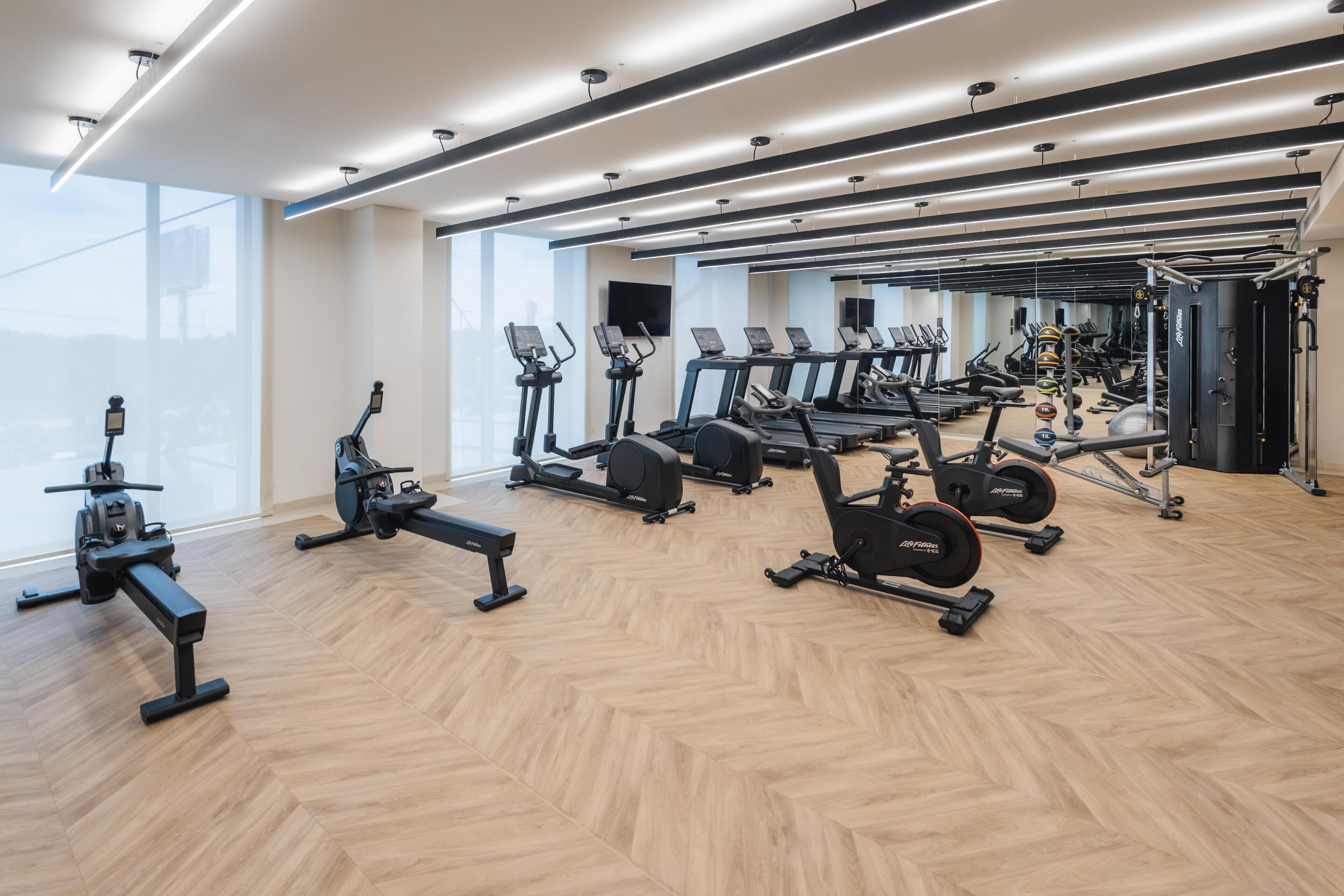 A modern gym with cardio machines, weightlifting equipment, and a large mirror.