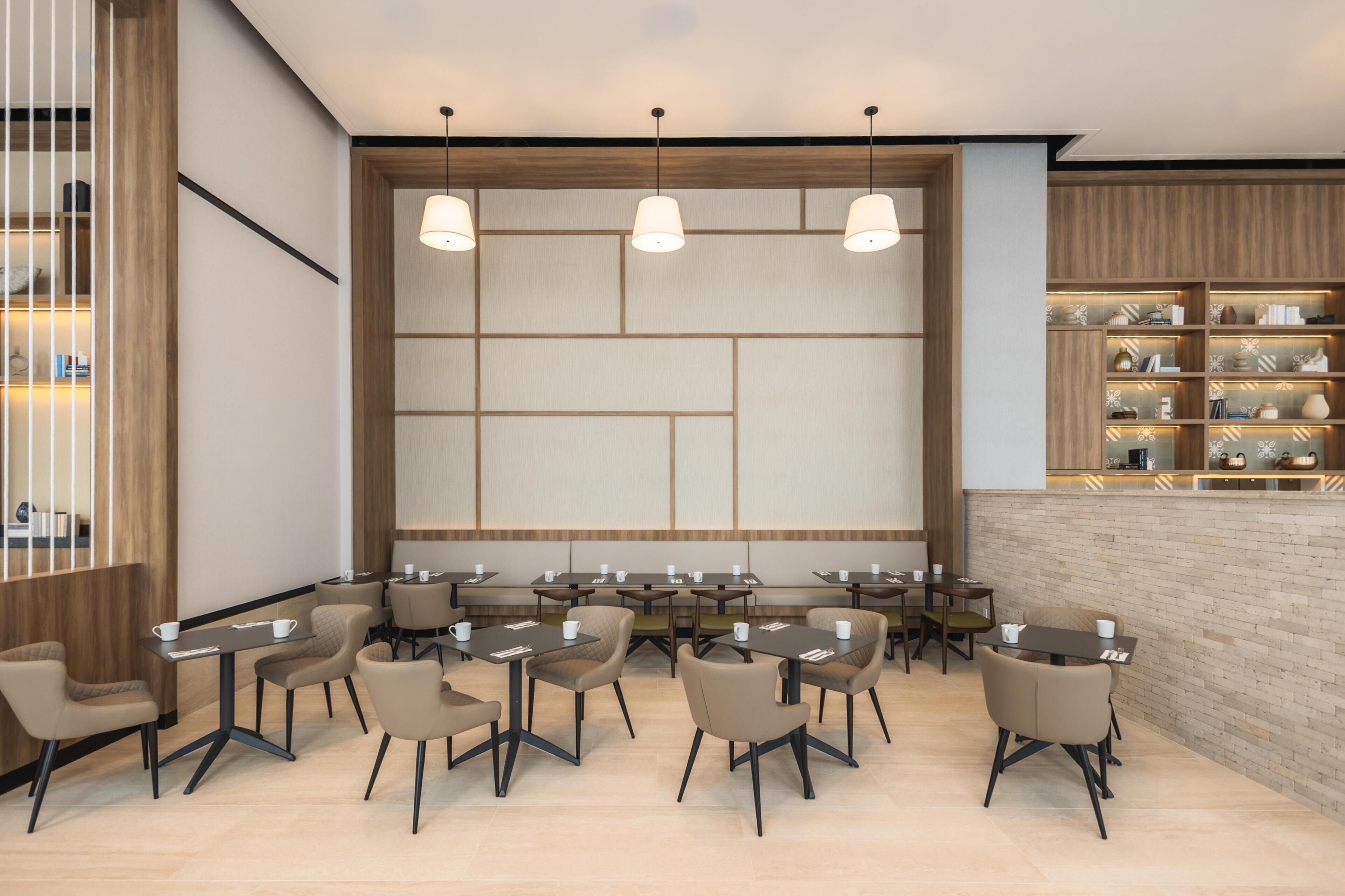 A modern dining area with multiple tables and chairs, a large wall with a geometric pattern, and a shelf with decorative items.