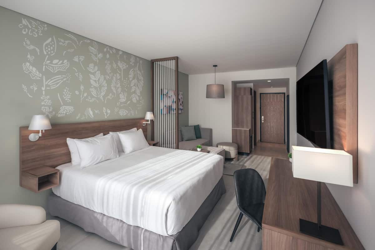 Ein modernes Hotelzimmer mit einem großen Bett, einem Schreibtisch, einem Stuhl, einem Fernseher und einer separaten Sitzecke mit einer Couch und einem kleinen Tisch.