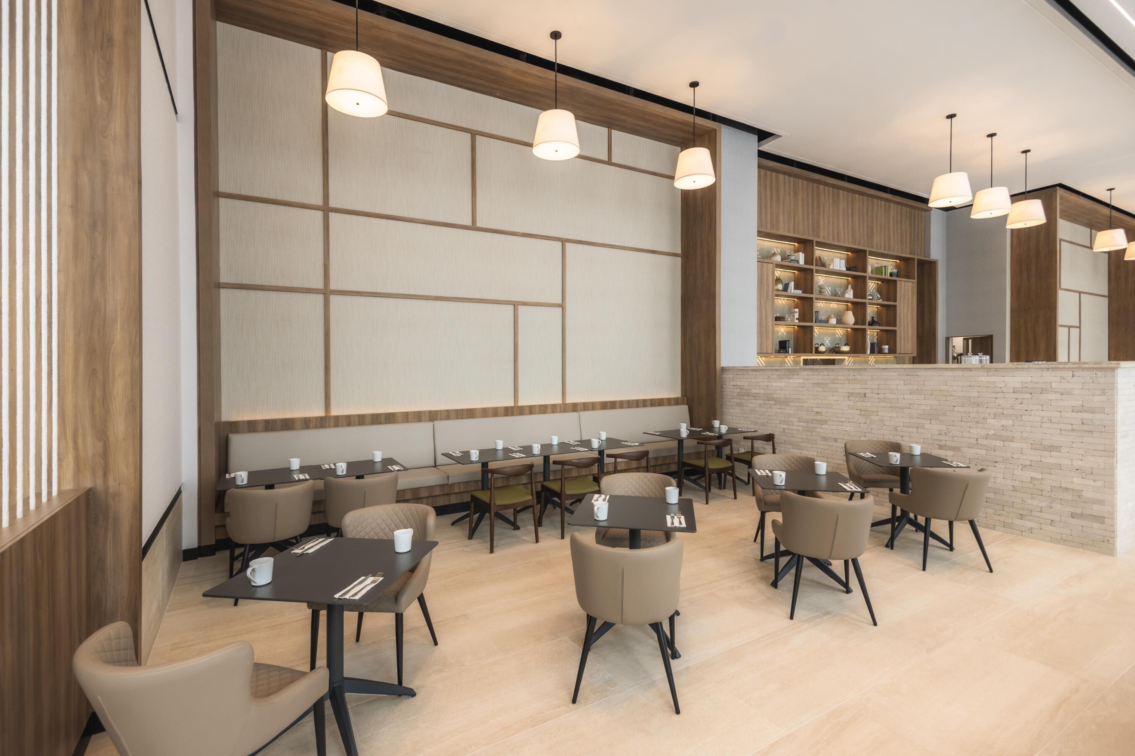 Un restaurante moderno con varias mesas y sillas, iluminación colgante y una pared de ladrillo decorativa.