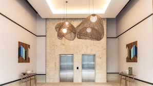 Eine großzügige Lobby mit zwei Aufzügen, Holzboden und hängenden Pendelleuchten.