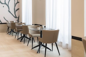 Un'area pranzo moderna con un tavolo lungo e sedie, una parete con un motivo alberi e ampie finestre con tende leggere.