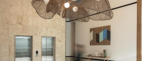 A spacious lobby with a herringbone floor pattern, a modern chandelier, and a wall-mounted abstract art piece.