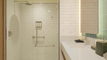 Une salle de bain moderne avec une douche à parois de verre, des carreaux blancs rectangulaires et un plan de toilette blanc agrémenté d’un porte-serviettes et d’un distributeur de mouchoirs.