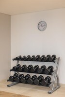 A wall-mounted clock and a multi-tiered dumbbell rack against a plain wall.